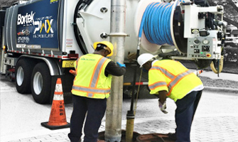 Workers shown lowering a sewer jetter hose into a manhole behind a Sewer Jetting Truck.