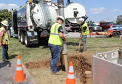 Workers using a hydro excavator to expose a buried utility line