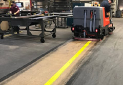 A rider floor scrubber in a factory with a clean streak behind it